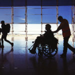 Aviation Service professional pushing handicapped passenger in a wheelchair through an airport.