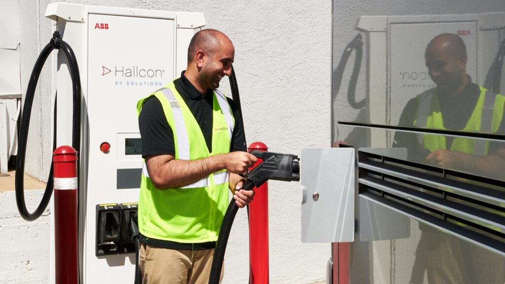 A man is plugging in a EV charger into a Hallcon bus.