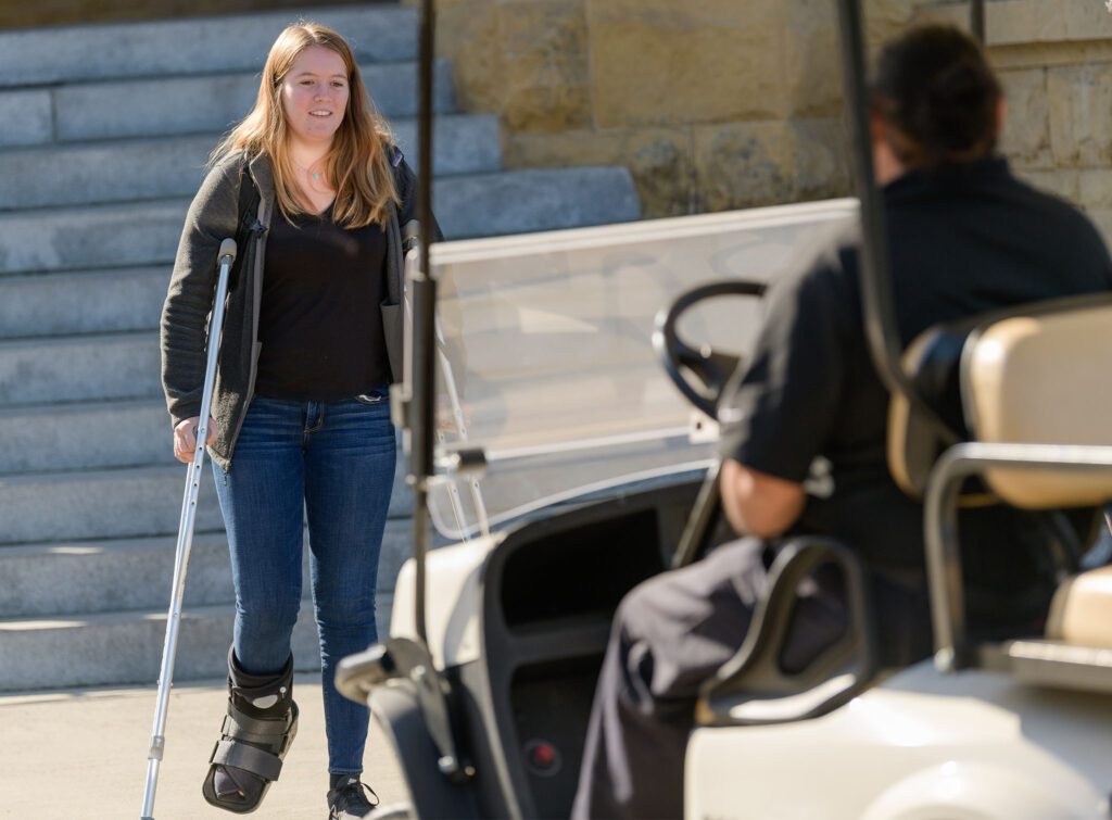 Girl on crutches walking to an on campus shuttle vehicle