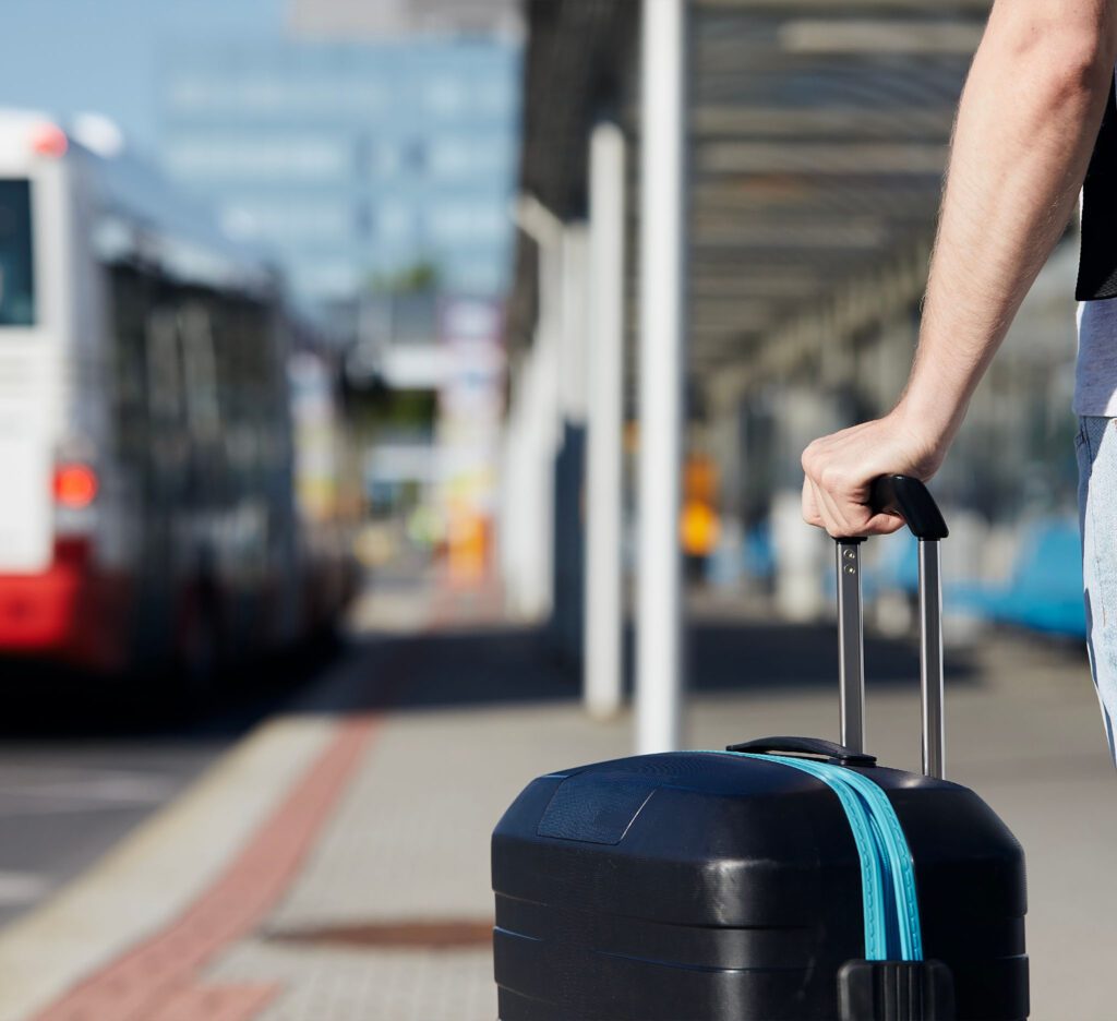 A passenger awaits being picked up, holding their luggage.