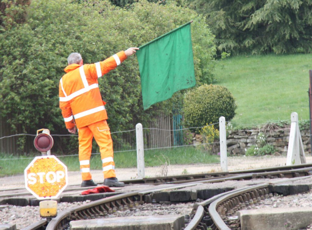 Hallcon railroad flagger standing by rails with a green flag.