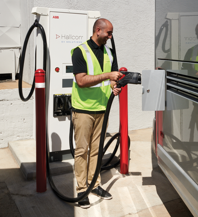 Hallcon employee smiling while charging an EV motorcoach